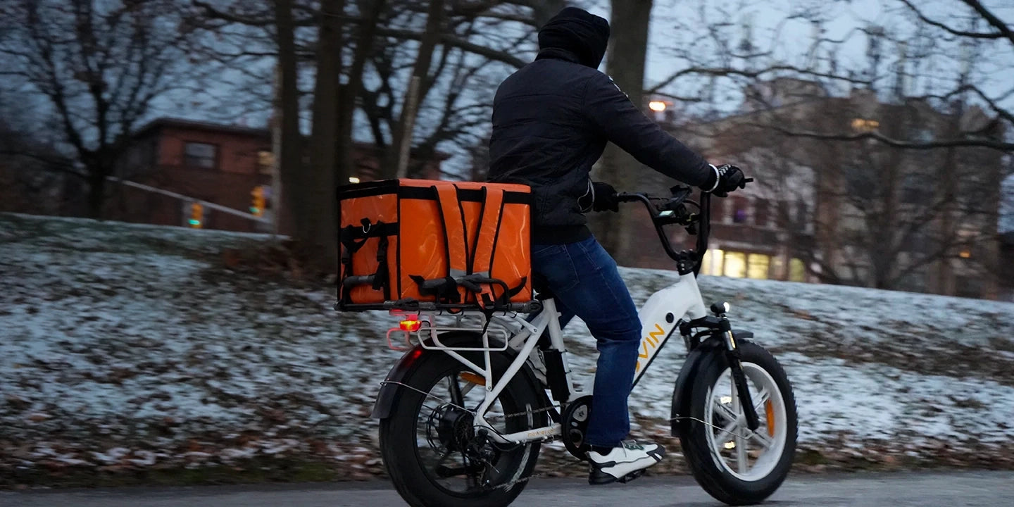Doordasher on a Movin' electric bike with an orange delivery bag in a snowy urban setting